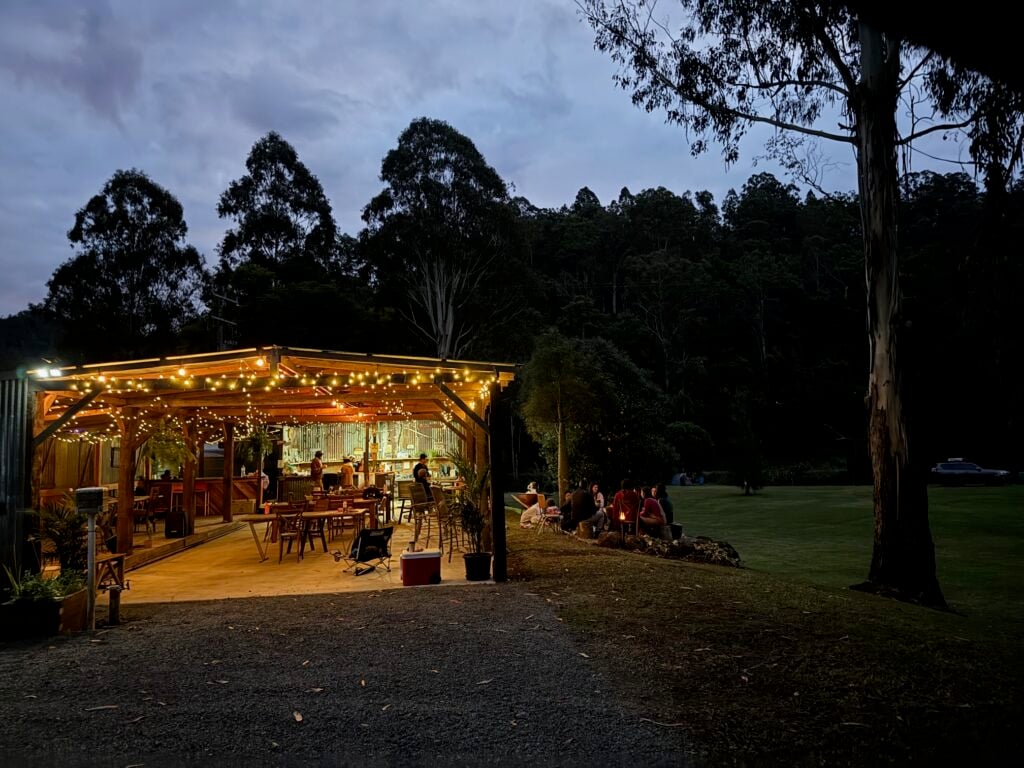 A wide shot of a rustic, open-air pavilion glowing with warm string lights at dusk