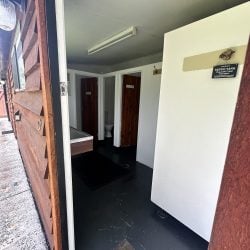 An open doorway leads into a public restroom area featuring dark floors, white walls, and wood-paneled stalls.