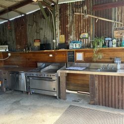 An outdoor, rustic commercial-style kitchen featuring corrugated metal walls and wood panelling.