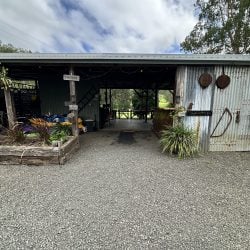 A rustic, open-air camp kitchen and storage shed with a corrugated metal exterior, set against a gravel foreground and a cloudy sky.