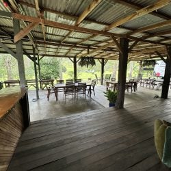 A perspective from the raised wooden deck looking out toward the communal dining area and the lush green landscape beyond the open-sided structure.
