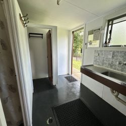 An interior view of a communal bathroom and shower facility featuring dark painted floors with black rubber drainage mats.