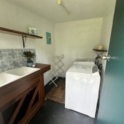 A simple, white-walled laundry room featuring a wood-framed double sink with blue patterned tiles and two top-loading washing machines.