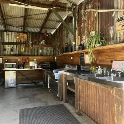 A rustic, indoor/outdoor camp kitchen featuring corrugated metal walls and roof, wooden counters with stainless steel sinks